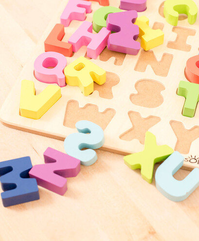 Buntes Holzpuzzle mit Buchstaben und Zahlen auf Teppich.